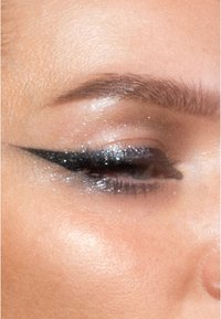 Párpado con delineador de ojos negro en alas, sombra de ojos plateada brillante y un ligero brillo en la piel, con pestañas y cejas definidas.