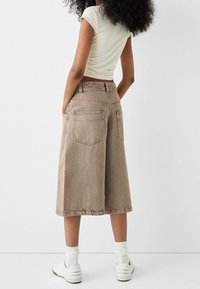 Culottes en denim marron avec une taille haute, des poches latérales et des poches arrière. Associés à des baskets blanches et des chaussettes à côtes.