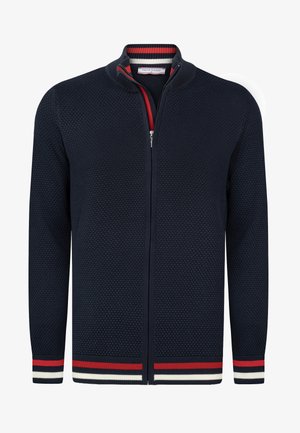 Granatowy kardigan zapinany na zamek, wykonany z teksturowanej dzianiny. Posiada stojący kołnierz oraz czerwono-biało-niebieskie paski na mankietach i dolnej krawędzi.