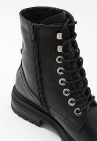 Bottine en cuir noir avec bout rond, fermeture à lacets, œillets argentés et fermeture éclair latérale, dotée d'une semelle en caoutchouc texturée.