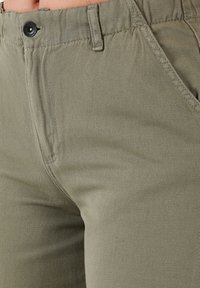 Olivgrüne Baumwollhose mit strukturiertem Finish, ausgestattet mit einem vorderen Knopfverschluss und seitlichen Taschen.