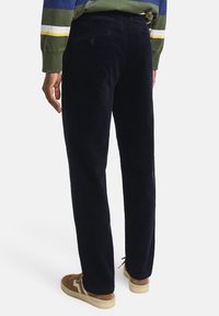 Pantaloni di velluto a coste blu navy con vestibilità dritta, dotati di una tasca posteriore con bottone. Abbinati a sneakers in suede marroni.