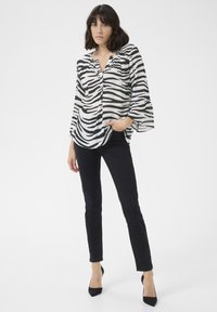 Blusa a maniche lunghe con motivo zebra in bianco e nero e scollatura a V, abbinata a jeans skinny neri e tacchi a punta neri.