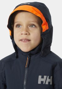 Námořnická modrá nepromokavá bunda s kapucí s oranžovým akcentem, plným zipem a velkým šedým logem, navržená pro venkovní použití dětí.