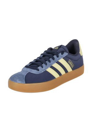 Low-Top Adidas Sneaker mit marineblauen und hellgelben Streifen, Gummisohle und Wildleder-Zehenkappe, dargestellt vor weißem Hintergrund.