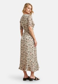 Maxi-Kleid mit Zickzackmuster in Pastellfarben. Kurze Ärmel, tailliert und mit gerafftem Saum. Getragen mit schwarzen Blockabsatzsandalen.