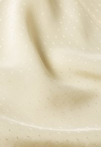 Tessuto crema chiaro con una texture liscia, caratterizzato da un sottile motivo a pois bianchi. Il materiale ha una leggera lucentezza e cade dolcemente.