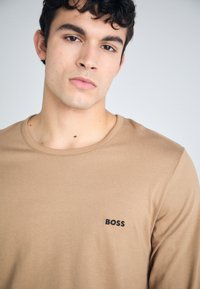 Rudas ilgomis rankovėmis marškinėliai, pagaminti iš minkštos medžiagos, su juodu "BOSS" logotipu kairiajame krūtinės gale ir apvaliu iškirpimu.