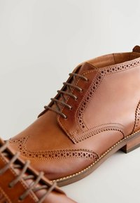 Brązowe skórzane buty eleganckie z tłoczeniem brogue, z okrągłym noskiem, sznurowanym zapięciem oraz niskim, warstwowym obcasem. Gładka tekstura i wypolerowane wykończenie.