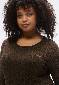 Rudonas ilgomis rankovėmis megztinis su leopardų raštu, ribuota tekstūra, scoop iškirpte ir mažuoju Levi's logotipu kairėje krūtinės pusėje.