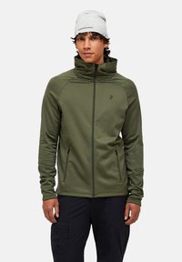 Giacca verde oliva con zip e colletto alto, realizzata in tessuto morbido. Presenta due tasche anteriori con zip e un dettaglio logo sul petto.