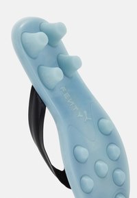 Blue sports cleat sole with conical studs and black upper strap, viewed from the bottom, showing traction design and Fenty branding.