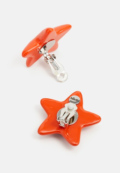 Bright orange star-shaped brooch with a glossy finish, featuring a silver metal clasp on the back and a small logo detail.