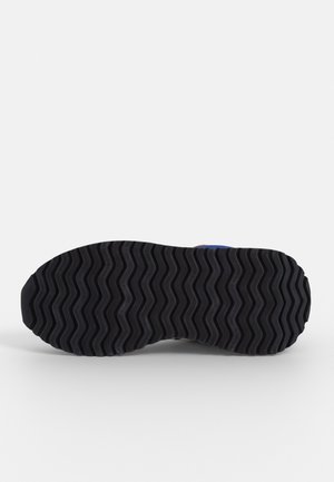 Sort gummisål på sneaker med zigzag-mønster, vist fladt mod en hvid baggrund.