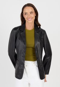 Zwarte leren blazer met een puntrevers, enkelvoudige knopen sluiting en zijzakken. Gecombineerd met een groene top en lichte broeken.