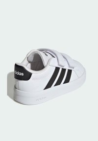 Bijele tenisice s Velcro trakama, crnim naglaskom na peti i tri crne pruge sa strane. Glatka tekstura i zaobljeni oblik.