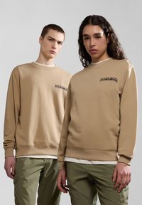 Felpe in cotone beige con polsini e orlo a coste, con un logo nero sul petto, abbinate a pantaloni cargo verdi.