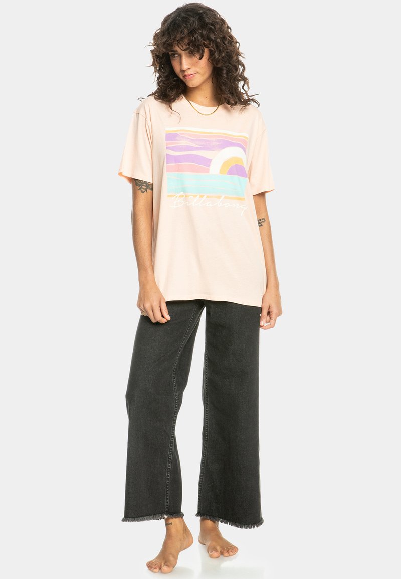 Vaaleanpunaista ylisuurta t-paitaa, jossa on grafiikka, jossa on pastelliväreissä aaltoja ja aurinko, yhdistettynä korkeavyötäröisiin mustiin leveisiin farkkuihin.