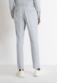 Pantaloni leggeri grigi con elastico in vita, due tasche posteriori con bottoni e orli arrotolati, abbinati a sneakers bianche.