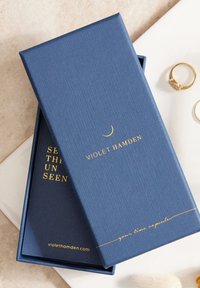 Boîte texturée bleu marine avec l'inscription dorée "VIOLET HAMDEN" et "votre capsule temporelle" à l'intérieur, avec un intérieur lisse.