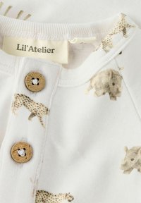 Biała bawełniana koszula z beżowymi nadrukami zwierząt, dwoma drewnianymi guzikami przy kołnierzyku, z naszywką „Lil'Atelier” wewnątrz.