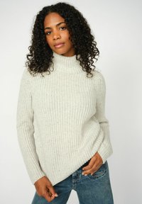Hellgrauer gerippter Pullover mit hohem Kragen, langärmlig und mit lockerer Passform, kombiniert mit blauen Jeans für einen lässigen Look.