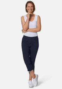 Marineblaue, taillierte Kurz-Hosen, kombiniert mit einem weißen, ärmellosen Oberteil und weißen Sneakers. Glattes Material ohne sichtbare Muster.