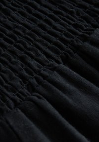 Tissu noir avec un design froncé et texturé. Il présente des rayures étroites et un matériau doux et extensible, mettant en valeur sa forme et son mouvement.