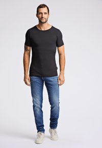 Zwarte aansluitende T-shirt met korte mouwen, ronde halslijn, gecombineerd met lichtblauwe spijkerbroek en witte sneakers. Eenvoudig ontwerp, gladde textuur.