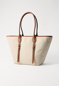 Borsa a spalla in tela beige con dettagli e manici in pelle marrone. Presenta una forma strutturata, spallacci regolabili e accessori in tonalità oro.