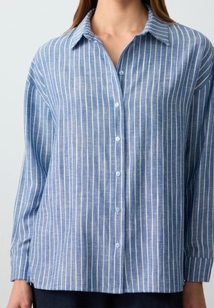 Camisa azul abotonada con rayas verticales blancas, mangas largas y cuello clásico, llevada por una persona.