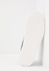 Baskets noires avec une surface texturée, dotées d'une semelle en caoutchouc blanche. La semelle présente un motif en grille pour l'adhérence.