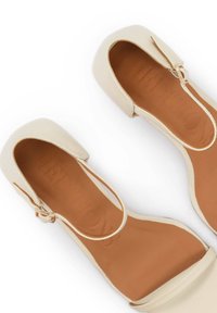 Beżowe damskie baleriny z odkrytymi palcami, paskami wokół kostki i złotymi klamrami, z brązowymi wyściółkami z poduszkami.