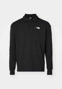 Svart långärmad polo av textil med strukturerad yta, med en klassisk krage och en vit broderad logotyp på vänster bröst.