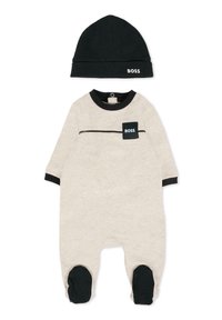 Combinaison en coton pour bébé de couleur beige avec des accents noirs, dotée d'une poche avec le logo "BOSS", à manches longues et accompagnée d'un bonnet noir assorti.