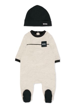 Combinaison en coton pour bébé de couleur beige avec des accents noirs, dotée d'une poche avec le logo "BOSS", à manches longues et accompagnée d'un bonnet noir assorti.