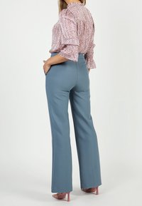 Světle modré kalhoty na míru se střihem rovného nohavice, které jsou kombinovány s růžovou květinovou blůzou s nařasenými rukávy a vysokým límcem.