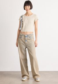 Lys beige ribbet crop top, løse lyseblå denimjeans med falming, og sølv sneakers; modell holder en sølvveske med stripete detaljer.