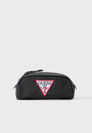 Trousse rectangulaire noire à fermeture éclair avec un patch logo GUESS USA rouge et blanc sur le devant, posée sur un fond clair uni.