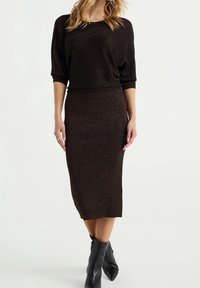 Brun, glittrig stickad topp med trekvartslånga ärmar i kombination med en matchande midikjol. Svarta spetsiga ankelstövlar fulländar outfiten.