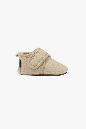 Pantofola in feltro beige con cinturino in velcro, superficie morbida, forma arrotondata e suola in suede marrone. Presenta un piccolo anello per facilitarne l'indossamento.
