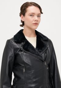 Black leather motorcycle jacket with a faux fur collar, zippered pockets, and a fitted design. Smooth texture and durable material.