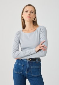 Maglia grigia chiara a maniche lunghe con scollo rotondo, abbinata a jeans blu a vita alta con due tasche posteriori e una cintura nera.