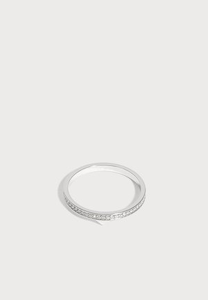 Bague anneau en argent avec de petites pierres claires incrustées entourant la surface extérieure sur un fond clair uni.