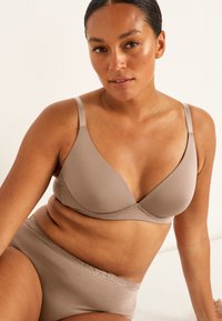 Vaurait beige vahega lohuge; mahaudised, pehmed, kolmnurksed tassid ja reguleeritavad rihmad, millele on lisatud sobivad õmblusvabad aluspüksid, millel on pitsäär.