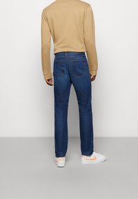Mörkblå denimjeans med rak benprofil, två bakfickor och subtil sömnad. Matchas med en beige långärmad skjorta och vita sneakers.