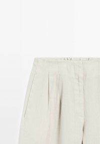 Lichtbeige linnen broek met een hoge taille, voorzien van voorpli?s en zijzakken. Een gladde textuur en een minimalistisch ontwerp.