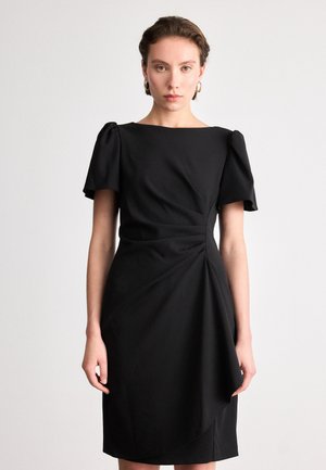 Robe noire avec de courtes manches bouffantes, un décolleté carré, un détail drapé à l'avant et une silhouette ajustée. Le tissu semble lisse et structuré.