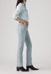 Ljusblå denimskjorta med spetsig krage och två bröstfickor, tillsammans med ljusblå raka jeans och svarta blockklack stövletter.