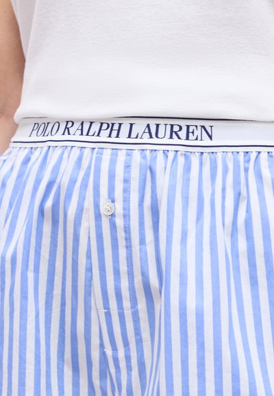 Λεπτομέρεια μέσης σε μπλε και λευκά κάθετα ριγέ μποξεράκια με ανοίγμα κουμπιών και λευκή ελαστική ζώνη μέσης με τη σήμανση "Polo Ralph Lauren".